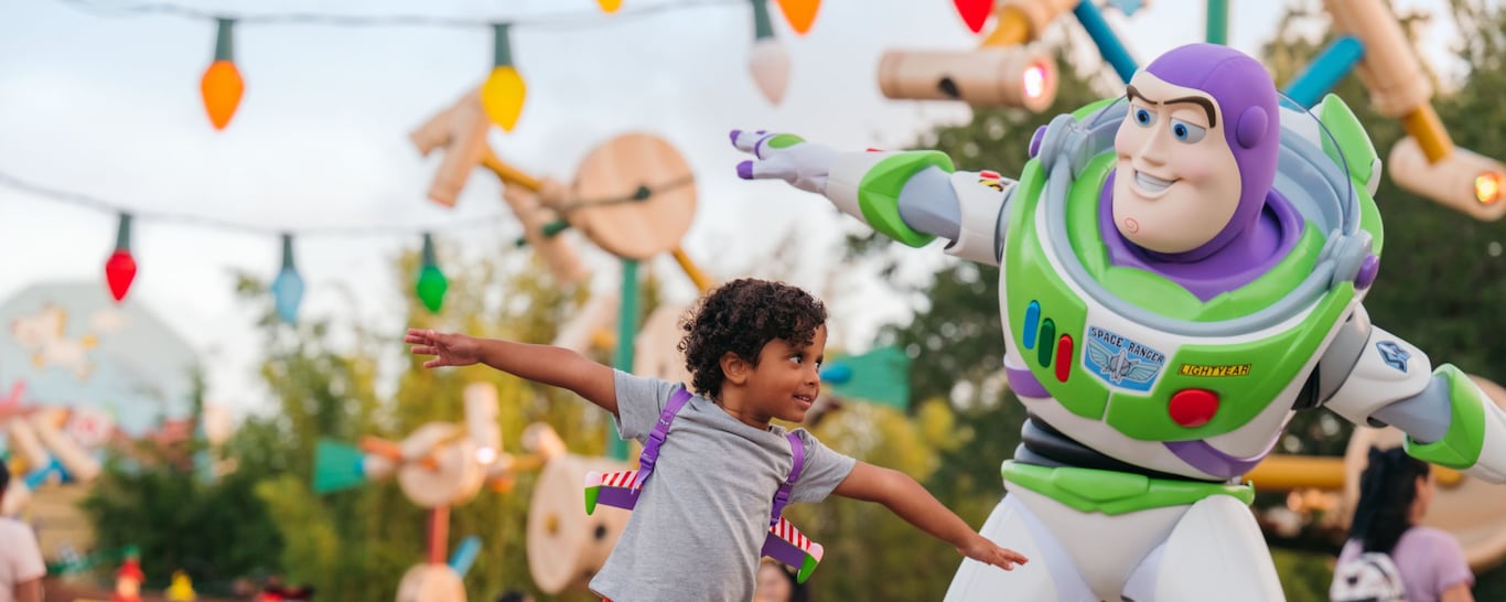 A young boy wearing space ranger gear standing next to Buzz Lightyear pretending to fly